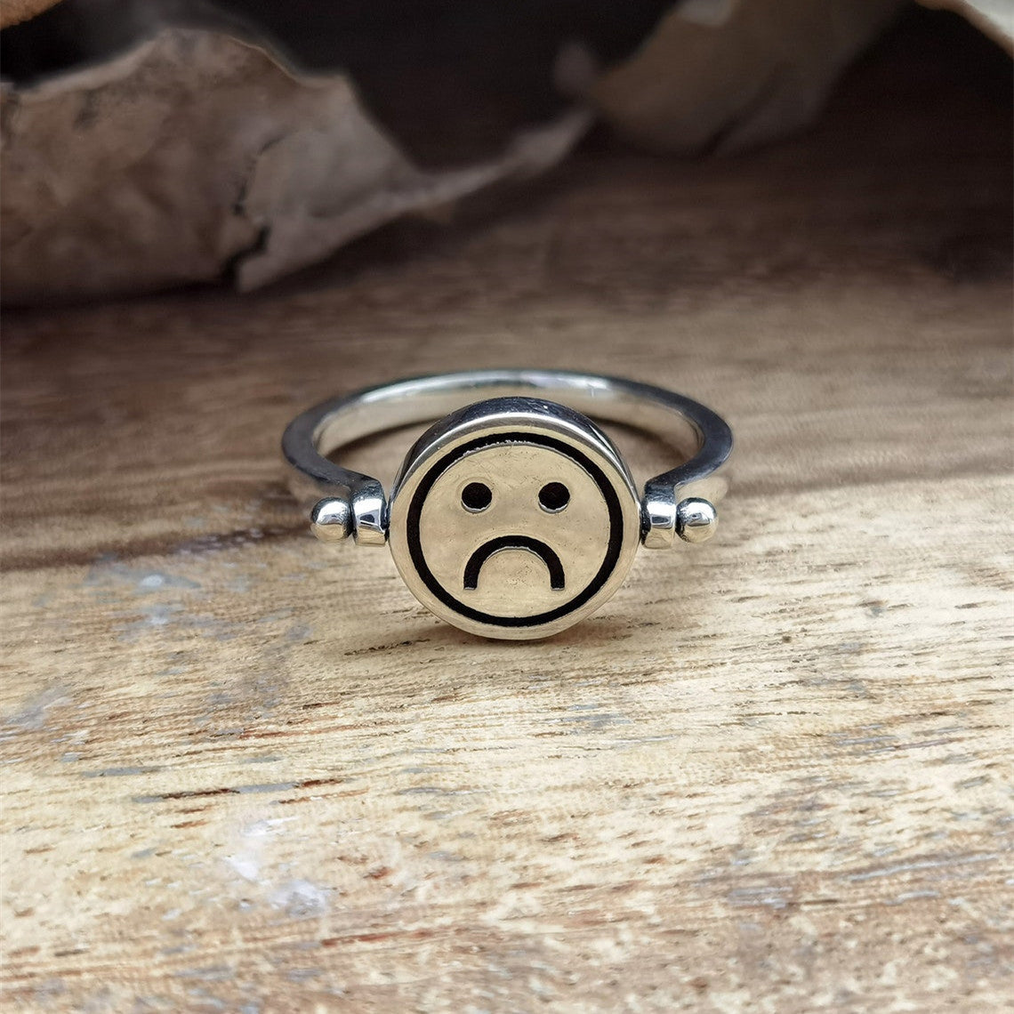 Velora Ring smiley face spinner ring with a sad face design on a wooden surface