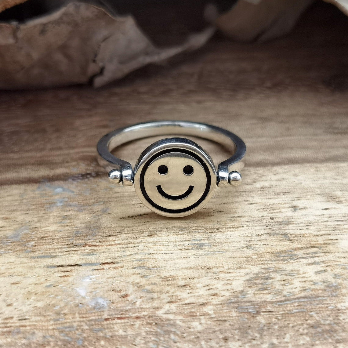 Velora Ring silver smiley face spinner ring on wooden surface with rustic background
