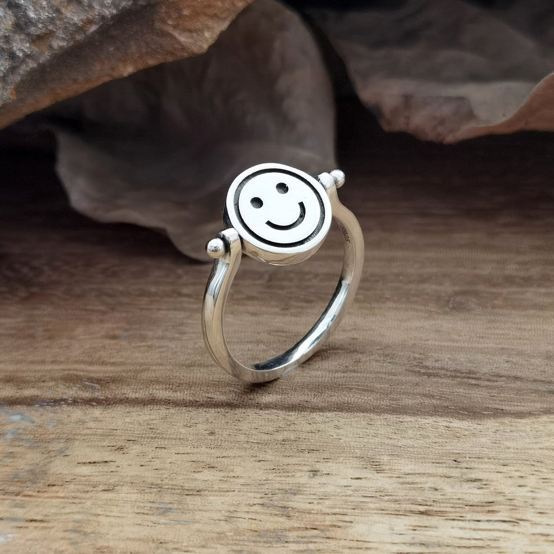 Velora Ring smiley face spinner ring in silver with a happy smiley face design on wooden background